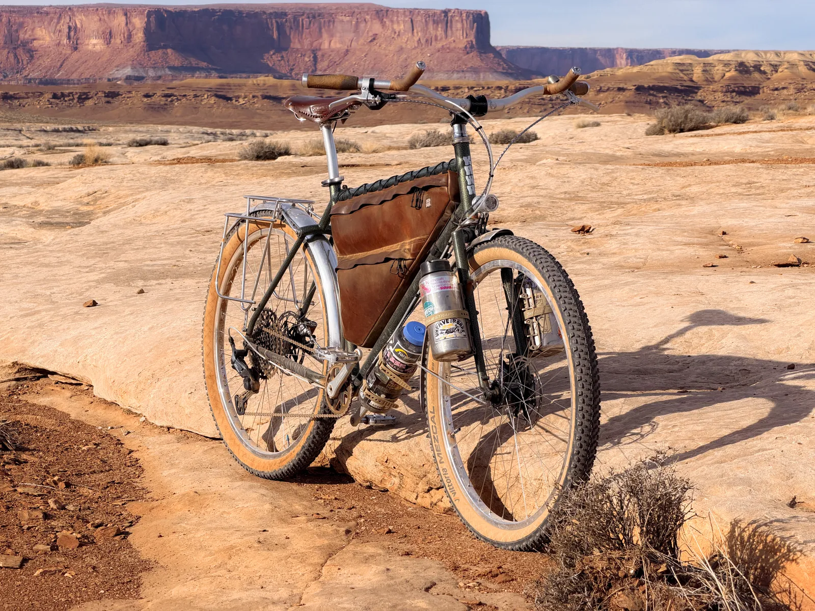 Rear three-quarter view of the Piolet showing the Campeur rack, drivetrain, and bag setup against Moab buttes
